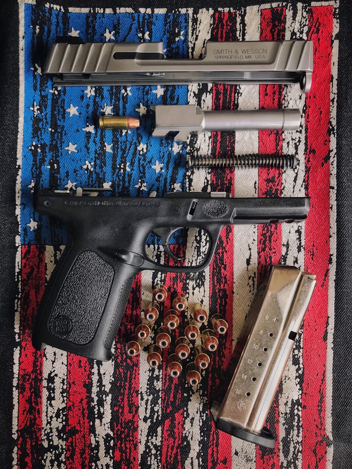 a-disassembled-gun-11794594 A disassembled firearm displayed on a textured American flag surface, showcasing parts and ammunition.