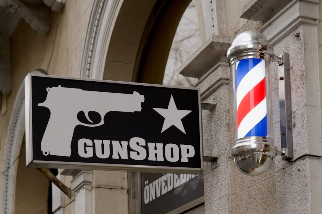 a-sign-that-says-gunshop-with-a-gun-hanging-from-the-side-of-a-building-9fbgkb3uj-a